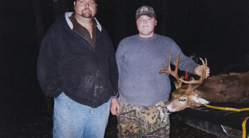 Billy Wagner and George Wagner standing next to a dead deer in the woods.